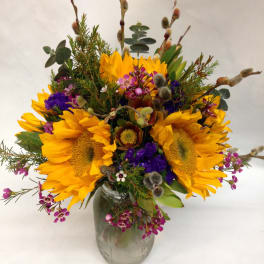 Mason jar arrangement of yellow sunflowers with purple and pink accent flowers