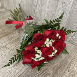 Hand-tied bouquet of red roses with small white daisies wrapped in clear cellophane and tied with a red ribbon.