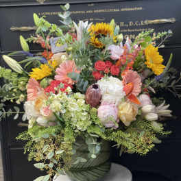 Mixed bouquet in a green patterned vase with sunflowers, roses, and lilies