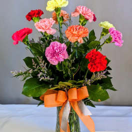 Colorful carnations in a glass vase with an orange ribbon