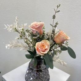 Peach roses in a dark glass vase with white filler flowers