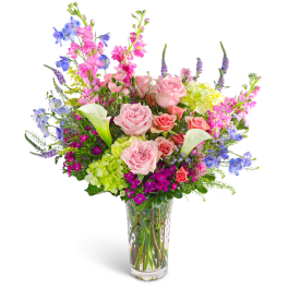 Mixed bouquet of pink roses, calla lilies, and blue flowers in a clear vase
