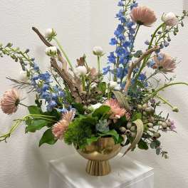 Mixed floral arrangement in a gold vase with blue and blush blooms