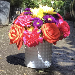 Bright mixed bouquet in a white textured vase with large orange and yellow blooms