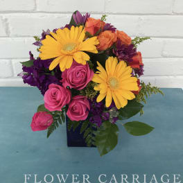 Bright mixed bouquet with yellow daisies, pink roses, and purple flowers in a dark vase