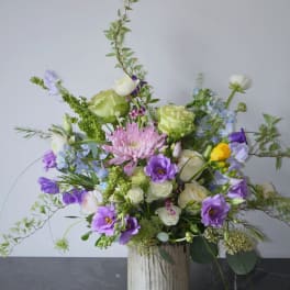 Mixed floral arrangement in a ribbed white vase with purple, white, and green blooms