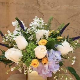 Bouquet of white roses, yellow roses, and purple flowers in a square vase