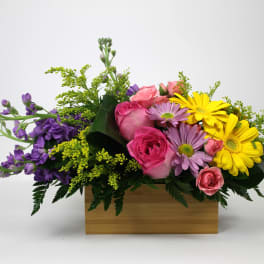 Mixed bouquet of pink roses, yellow daisies, and purple flowers in a wooden box