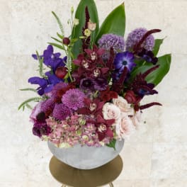 Purple and blush floral arrangement in a round white vase