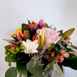 Mixed bouquet with pink lilies, roses, and white blooms in a glass vase