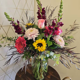 Mixed bouquet in a glass vase with sunflowers, gerbera daisies, and snapdragons