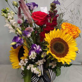 Mixed bouquet with sunflowers, roses, and purple blooms in a glass vase