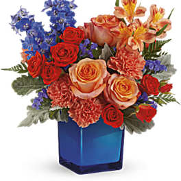 Mixed bouquet of roses, carnations, and blue flowers in a blue vase