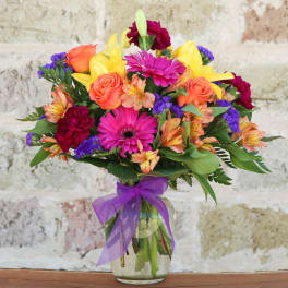 Colorful mixed bouquet in a glass vase with a purple ribbon