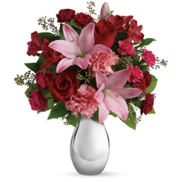 Red and pink lilies, roses, and carnations arranged in a silver vase