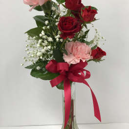 Red roses and pink carnations in a clear glass vase with a red ribbon