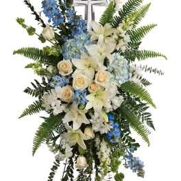 Standing funeral spray with white lilies, roses, and blue flowers on a cross easel