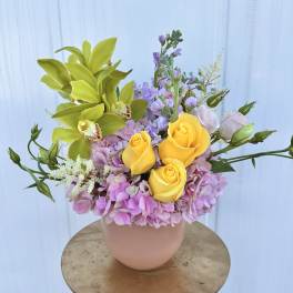 Bouquet of yellow roses, green orchids, and pink hydrangeas in a blush vase