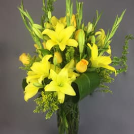 Yellow lilies and roses arranged in a clear glass vase