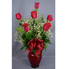 Red roses in a red vase with baby's breath and a ribbon bow