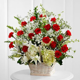 Basket arrangement of red roses, white lilies, and pale hydrangeas