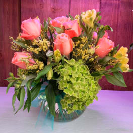 Pink roses and green hydrangea in a glass vase with yellow filler flowers
