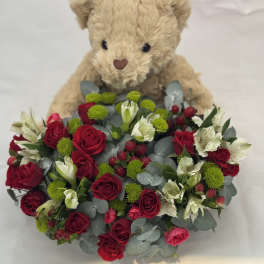 Teddy bear holding a bouquet of red roses and white flowers
