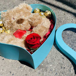 Teddy bear and chocolates in a turquoise heart-shaped box with a red rose