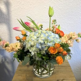 Mixed bouquet with blue hydrangea, orange roses, and pink tulips in a glass vase