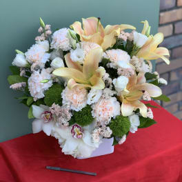 Mixed bouquet of lilies, carnations, and orchids in a white container