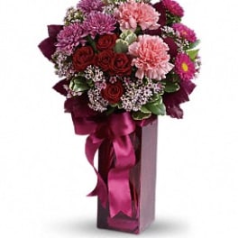 Bouquet of red and pink flowers in a tall vase with a magenta ribbon