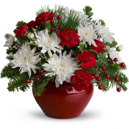 Red and white flowers in a red vase with evergreen accents