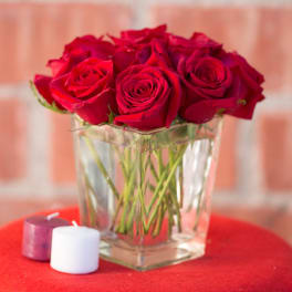 Red roses in a clear glass vase with two small candles nearby