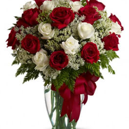 Red and white roses in a clear glass vase with a red ribbon
