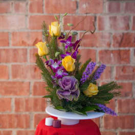 Purple and yellow floral arrangement on a white pedestal stand