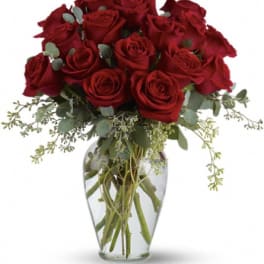 Red roses arranged in a clear glass vase with airy greenery