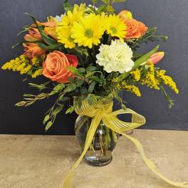 Bouquet of yellow daisies, orange roses, and white carnations in a glass vase
