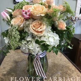 Peach roses and white hydrangeas in a glass vase with ribbon