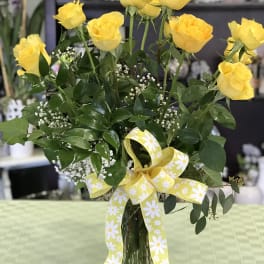 Yellow roses in a glass vase with a yellow daisy ribbon