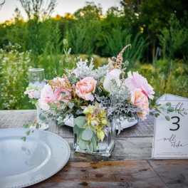 Pastel floral centerpiece in a clear glass vase on a table with a place card