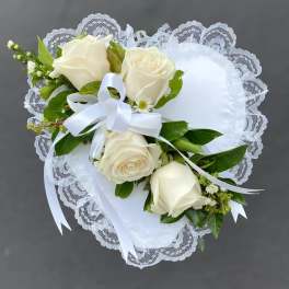White heart-shaped lace pillow adorned with ivory roses and a white ribbon bow.