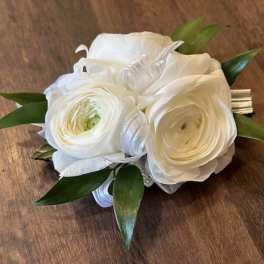 White ranunculus corsage with green leaves and silver ribbon