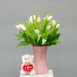 Pink tulips in a pink vase with a small teddy bear holding a heart