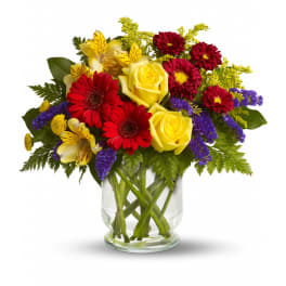Mixed bouquet of yellow roses, red daisies, and purple flowers in a glass vase
