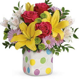 Bouquet of red roses, yellow lilies, and lavender daisies in a polka-dot vase