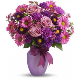 Pink and purple roses, daisies, and carnations in a lavender vase with a matching ribbon bow