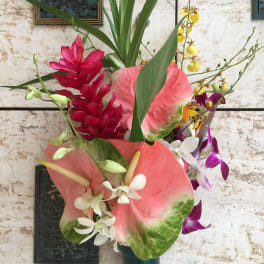 Tropical floral arrangement with pink anthuriums, orchids, and red blooms in a vase
