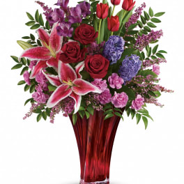Mixed bouquet of red, pink, and purple flowers in a red glass vase