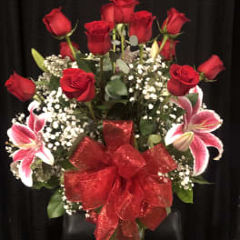 Red roses and pink lilies arranged in a glass vase with a red bow.