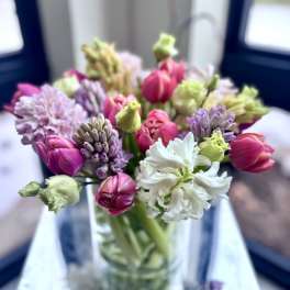 Mixed bouquet of pink tulips and pastel hyacinths in a clear glass vase.